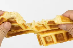 A waffle being torn down the middle by hand to test its consistency. This waffle was baked for 5 minutes.