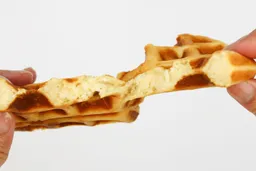 A waffle, baked for 5 minutes, is torn by hands to test for its consistency. The interior of the waffle is revealed.