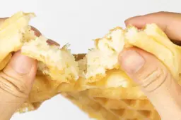 The waffle produced by the Cuisinart WAF-F20P1 is being torn by hand to test for its consistency and texture.