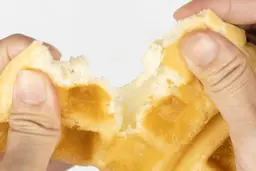 The waffle is being torn by hands to test its consistency and texture.