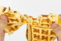 A waffle baked for 7 minutes being torn down the middle by hands in order to test it for consistency and texture.