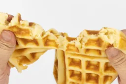 A waffle baked for 7 minutes being torn down the middle by hands in order to test it for consistency and texture.