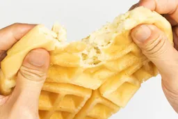 A waffle baked for 8 minutes being torn down the middle by hand to test it for its consistency and texture.