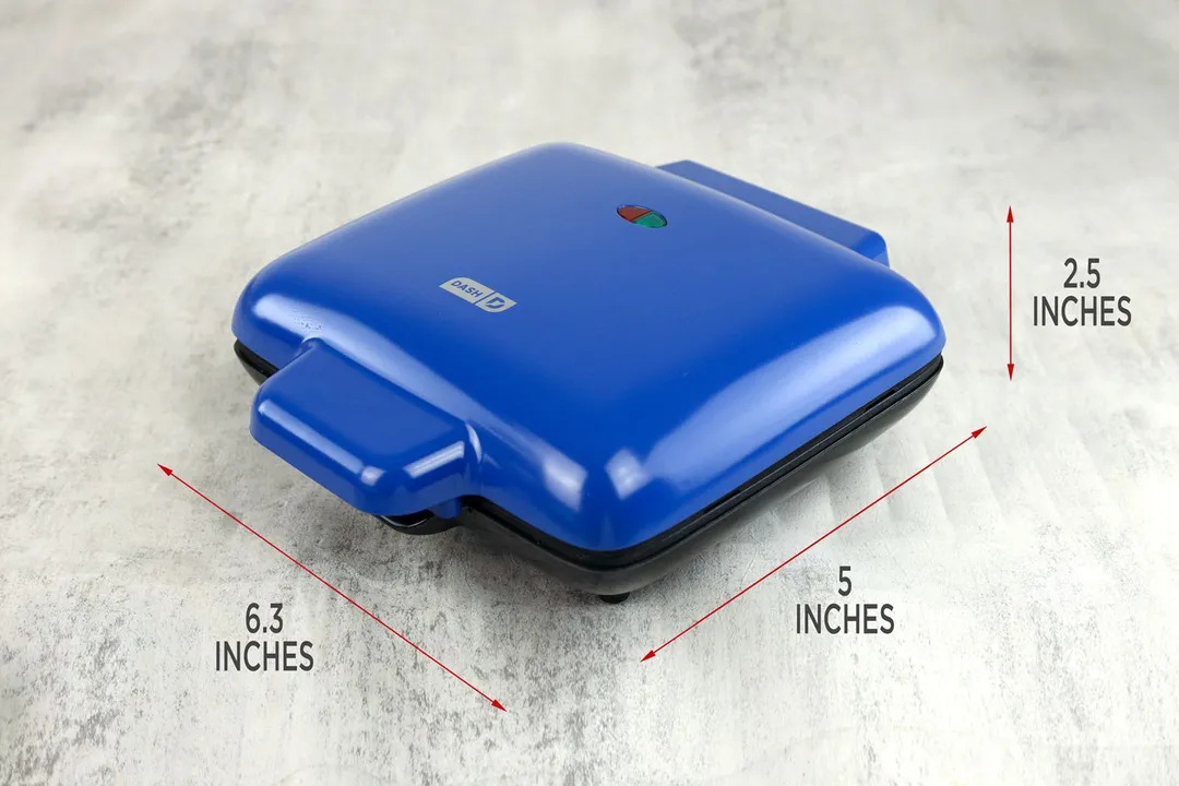 A side profile of the Dash No-Drip Belgian waffle maker. It has a blue plastic lid and black-painted base.