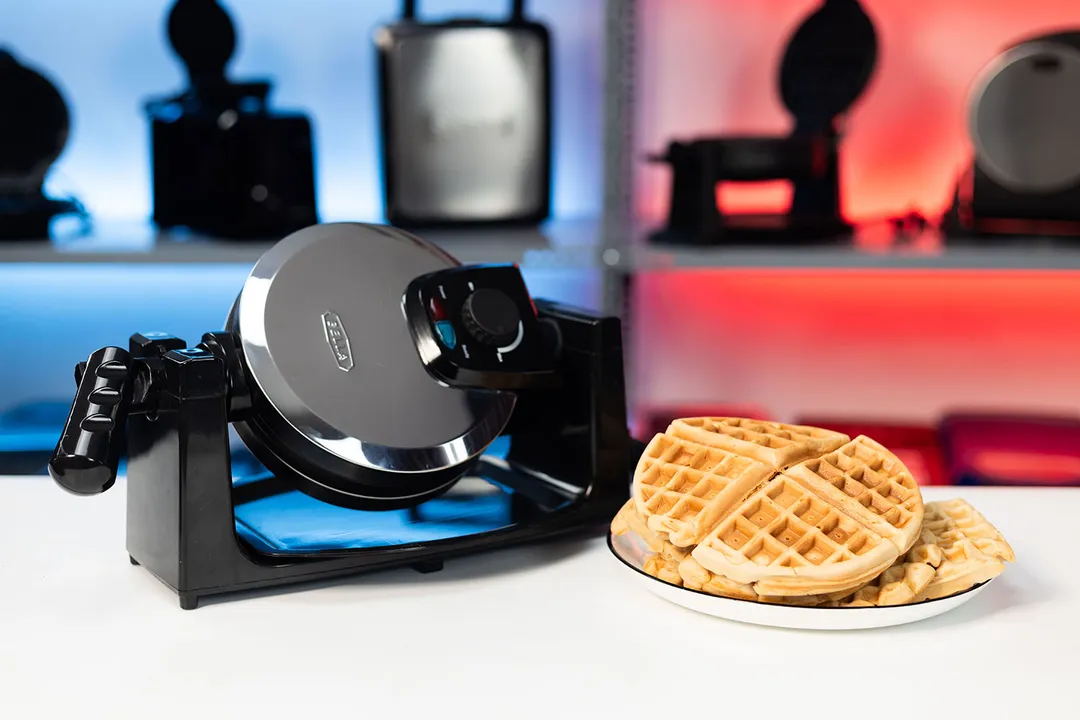 Bella 13991 waffle maker rotated slightly on its base next to a plate of fresh golden-brown waffles.