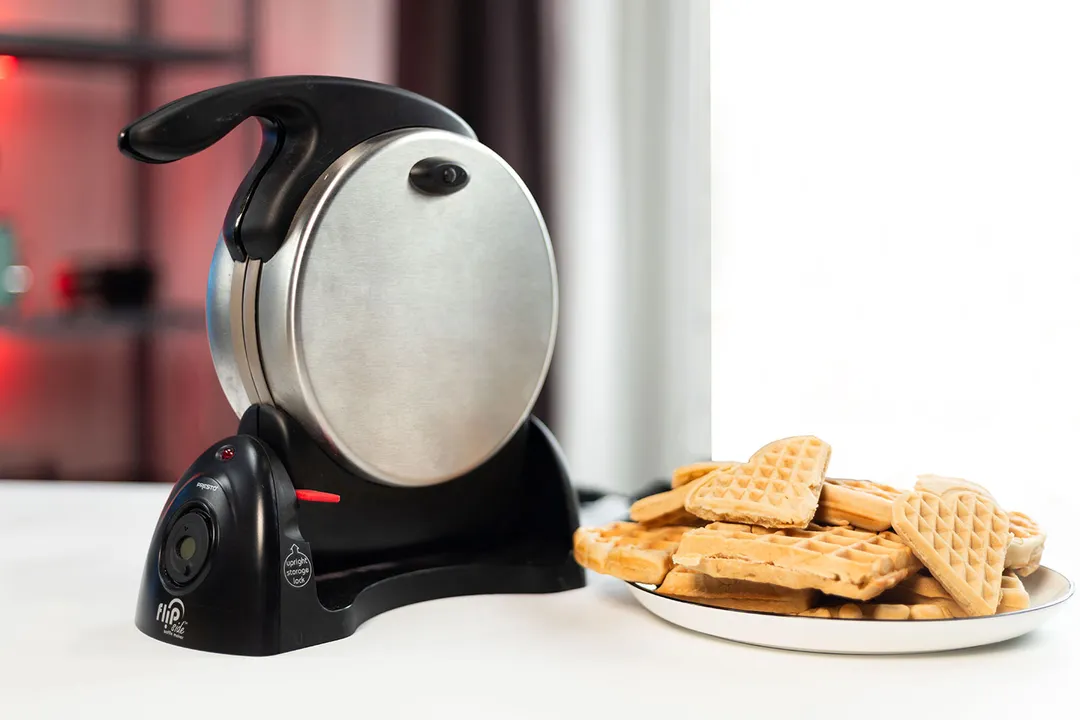 Presto Flipside waffle maker standing upright on a white countertop beside a plate of freshly-baked waffles.