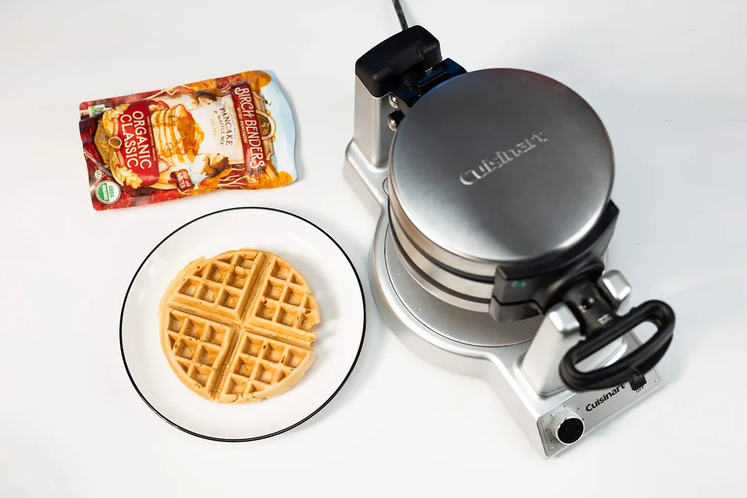 Cuisinart WAF-F20P1 waffle maker on a white countertop next to a plate with a single waffle and a sealed bag of Birch Benders instant waffle mix. 