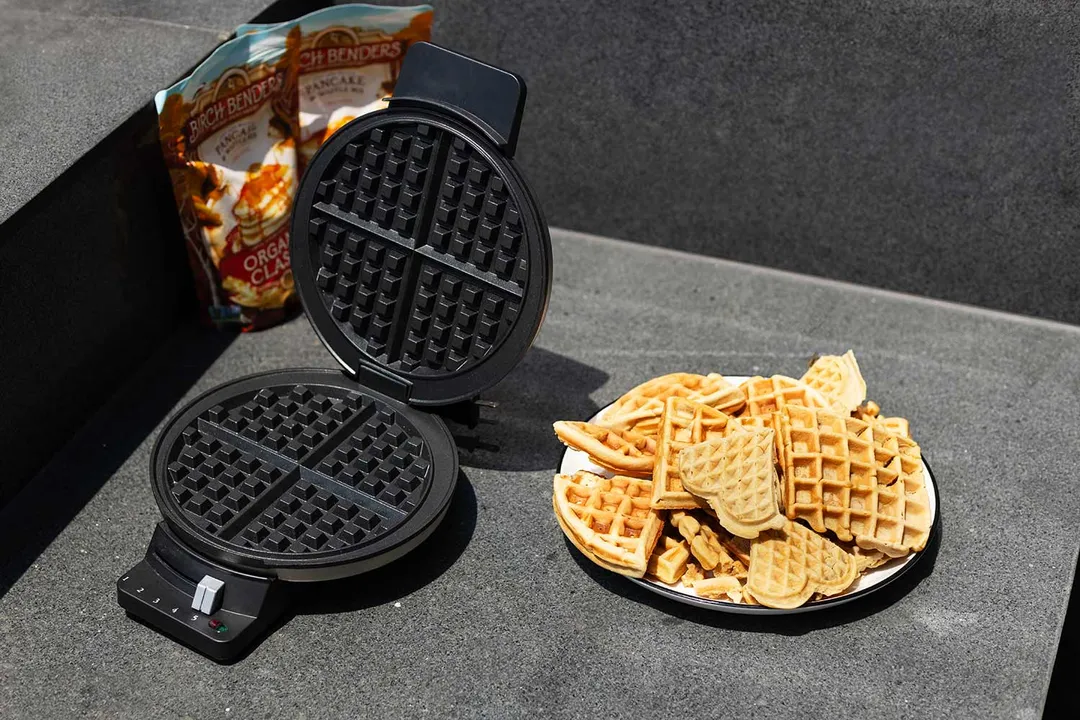 Cuisinart waffle maker next to a plate of golden-brown waffles on slate grey surface.