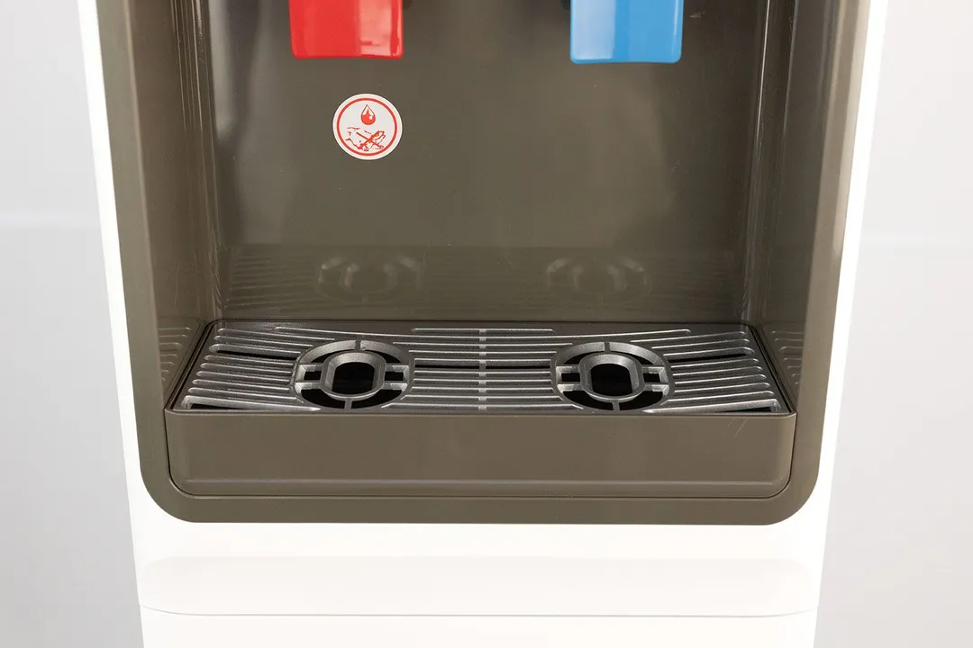 A drip tray seen below a partial view of two dispensing levers on a water cooler dispenser.