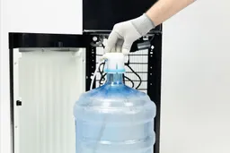 A cap being placed onto the top of a bottle standing in front of a water cooler dispenser.