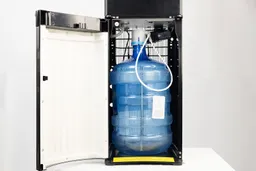 An open cabinet door of a water cooler dispenser with a bottle positioned inside.