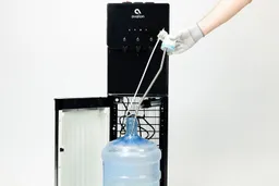A water probe or water needle being inserted into a bottle standing in front of a water cooler dispenser.