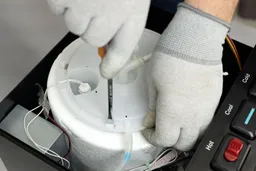 A flat screwdriver being used to loosen the clip on the lid of a cold water tank inside a water cooler dispenser. 