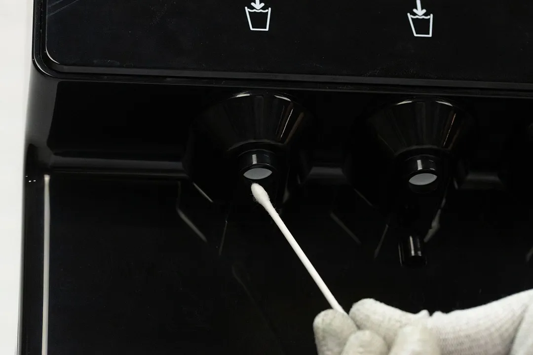 A Q-tip cotton swab being used to clean inside the water spout of a water cooler dispenser.