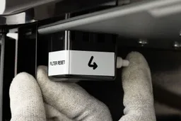A hand pressing a filter reset button on a water cooler dispenser.