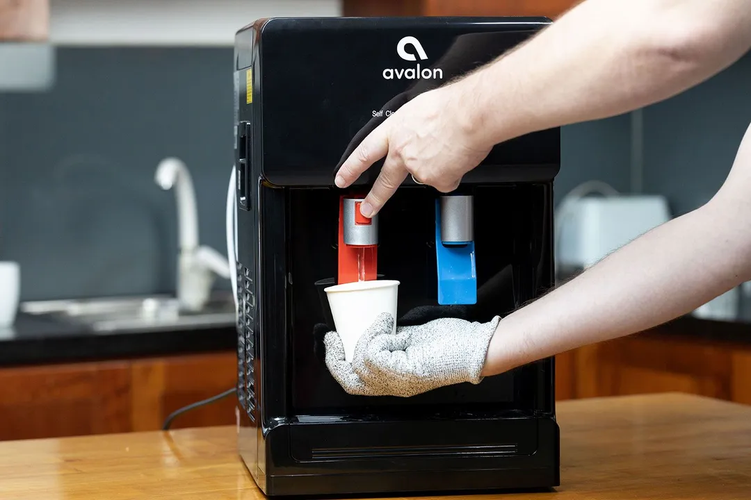  A gloved hand dispensing hot water from a water cooler dispenser by operating the hot water safety switch.