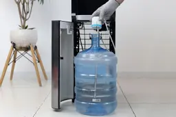 A water straw being placed into a 5-gallon water bottle in front of a bottom-loading water cooler dispenser.