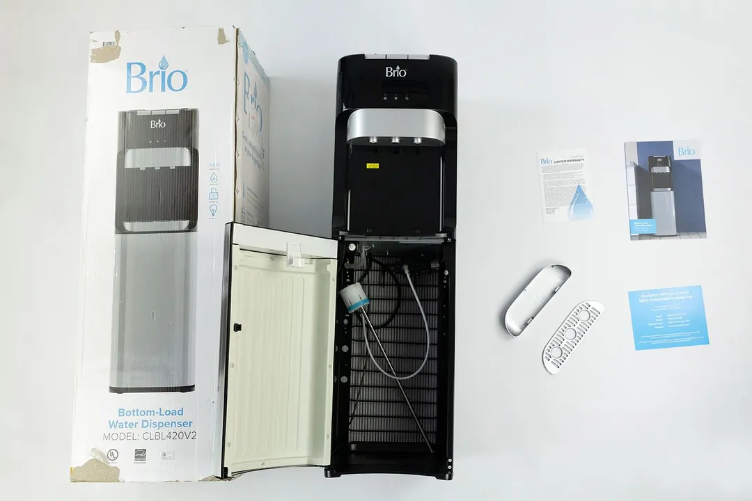 The unboxed Brio 400 water cooler dispenser with an open cabinet door, and the drip tray plus bundled literature to the side.