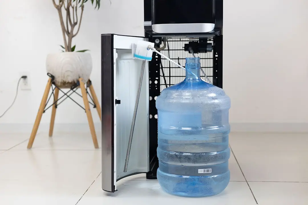Water straw hanging on the hook of the cabinet door of a bottom-loading water cooler dispenser while switching bottles.