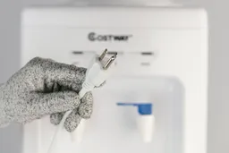 A gloved hand showing the plug of the Costway freestanding water cooler dispenser with the panel faded into the background.