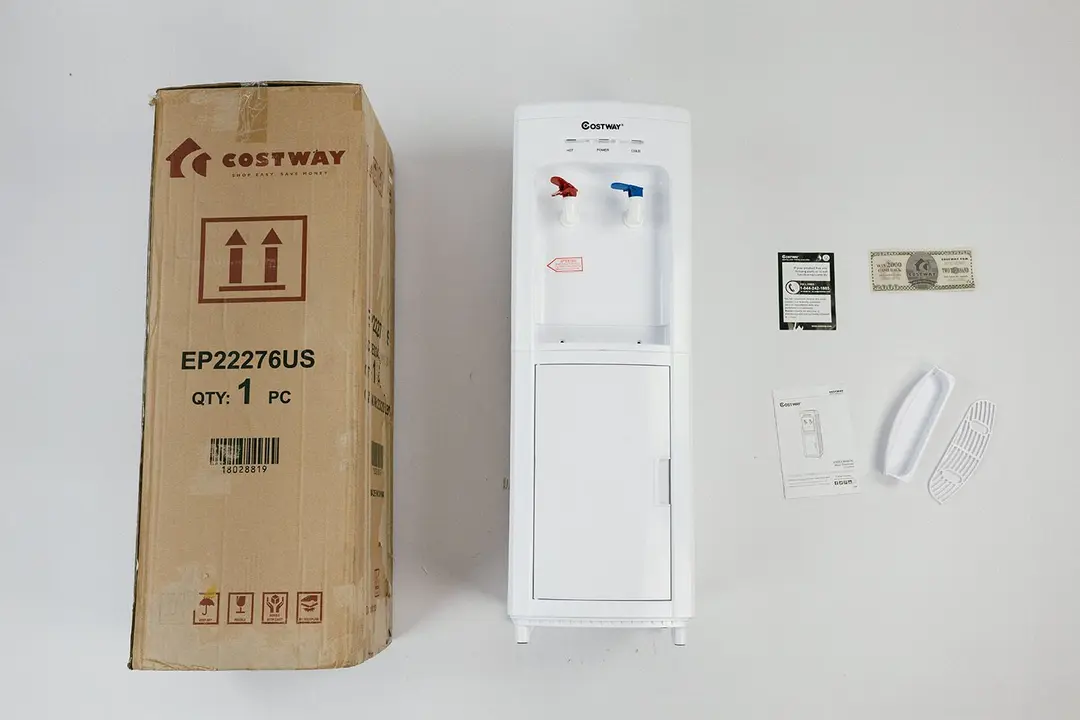 The Costway 5-gallon water cooler dispenser standing next to its box with the drip tray and included literature to one side