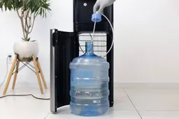 A gloved hand inserting or removing a water straw for a 5-gallon jug of a bottom-loading water cooler dispenser.