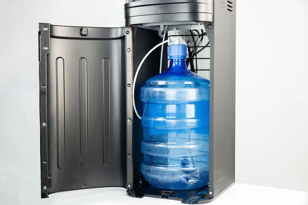A water bottle resting inside the cabinet of a bottom-loading water cooler dispenser with the cabinet door open. 