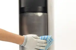Cleaning the stainless steel front of a water cooler dispenser.