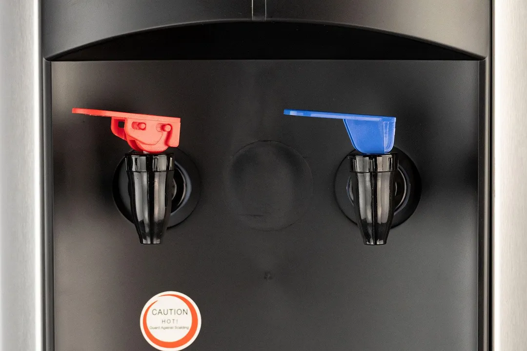 Close up of hot and cold water cooler dispenser taps with faucet-type levers. The left tap is red and the right is blue.