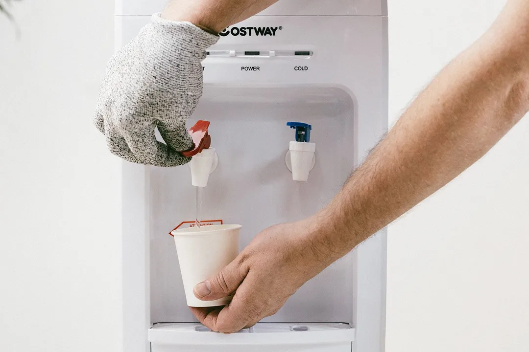 A gloved hand dispensing hot water from the Costway water cooler dispenser
