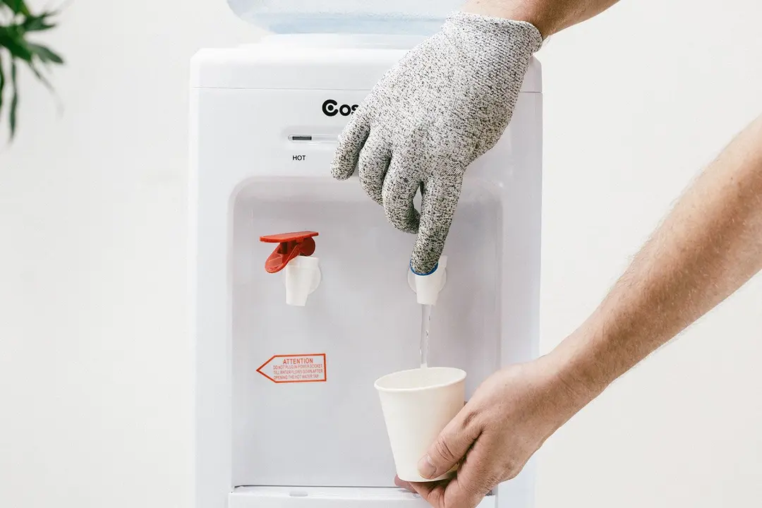A gloved hand dispensing old water from the Costway 5-gallon water cooler dispenser