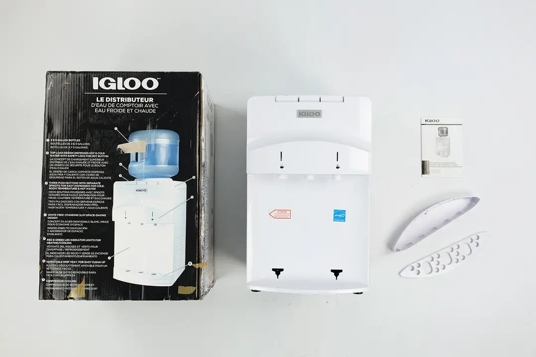 The unboxed Igloo countertop water cooler dispenser with the included drip tray and user manual shown on the far right.