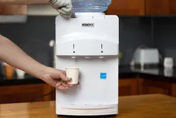 A person dispensing hot water from the Igloo hot and cold water cooler dispenser.