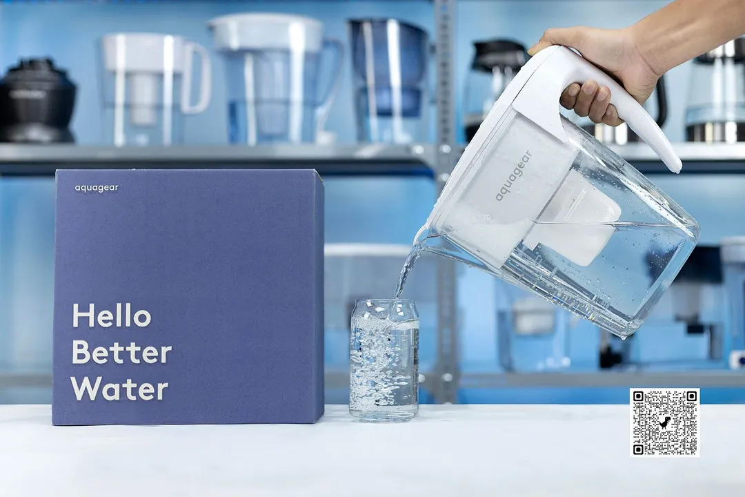 a hand holding the Aquagear water filter pitcher and pouring water into a glass, cardboard box