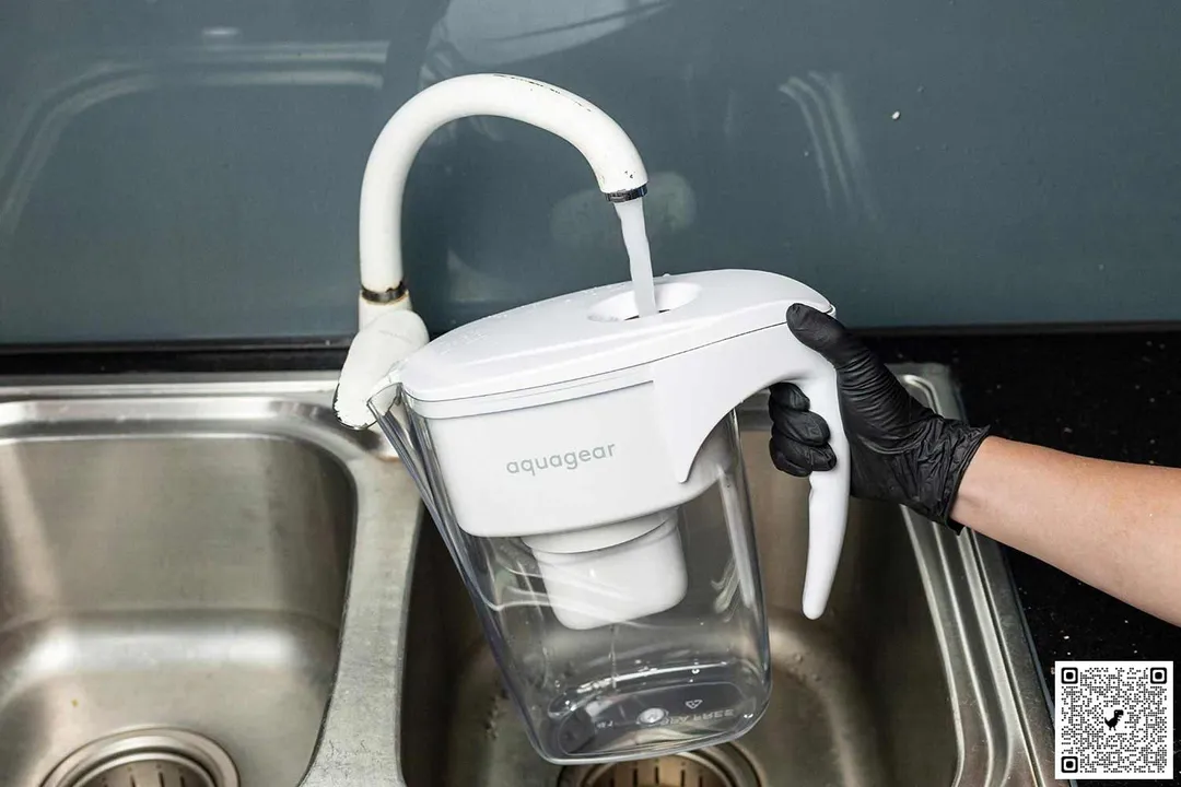 gloved hand holding Aquagear pitcher to refill at sink faucet