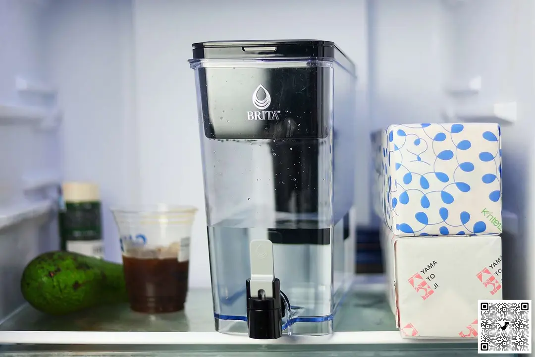 The Brita UltraMax 27 cup water filter dispenser on a fridge shelf, an avocado and glass of coffee to its left, two paper boxes to its right