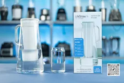 The LifeStraw Pitcher (7 Cup), a glass of water, the pitcher package box, a shelf full of blenders in the background