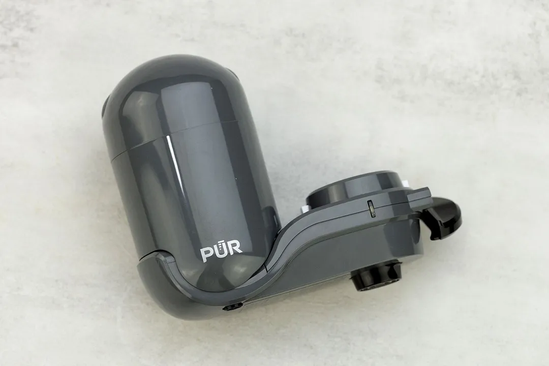 The grey, plastic PUR Plus FM2500V faucet-mount filter on its side on a grey table.