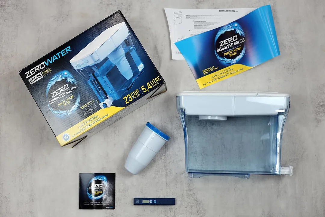 The ZeroWater 23 cup water filter dispenser lying next to its cardboard box, the instruction manual, promotional leaflet, filter piece, and TDS meter