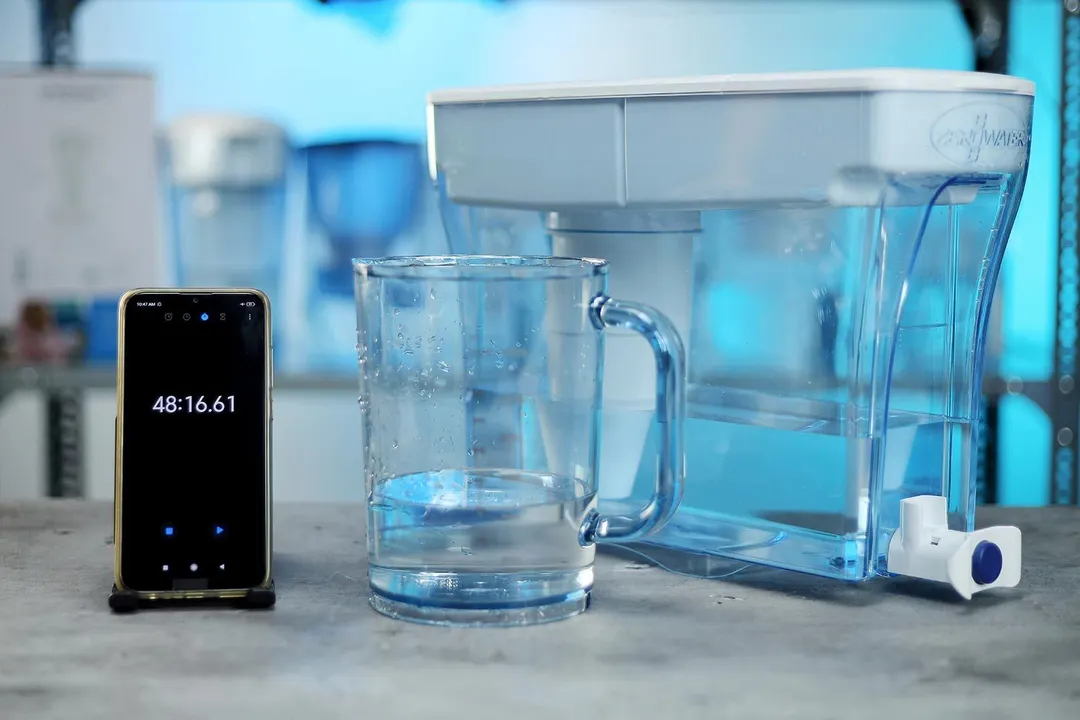 The ZeroWater 23 cup water filter dispenser next to a smartphone timer and a glass that contains water
