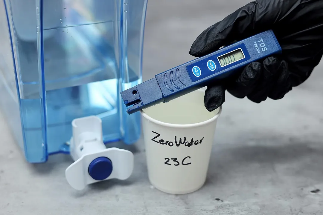 Hand holding TDS meter over cup labeled ZeroWater 23 C next to the dispenser